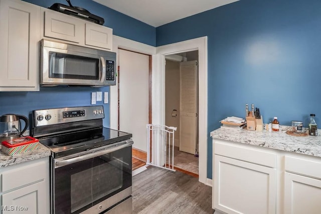 kitchen featuring white cabinets, light stone counters, stainless steel appliances, and hardwood / wood-style flooring