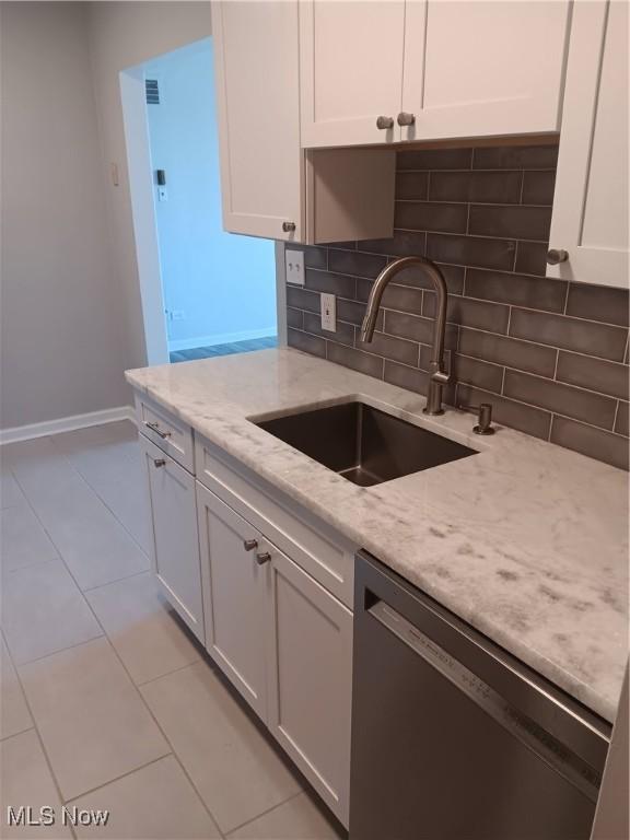 kitchen featuring black dishwasher, decorative backsplash, light stone countertops, white cabinets, and sink