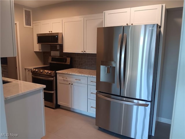 kitchen featuring backsplash, light tile patterned floors, light stone countertops, appliances with stainless steel finishes, and white cabinets