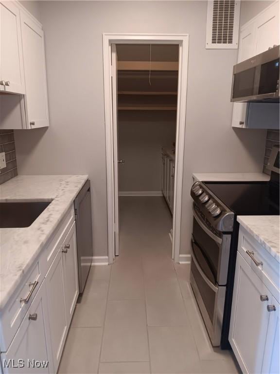 kitchen featuring appliances with stainless steel finishes, white cabinetry, and light stone countertops