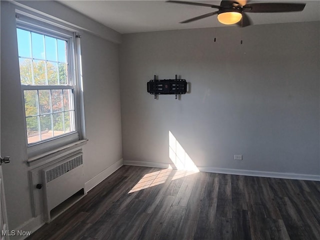 spare room featuring ceiling fan, dark hardwood / wood-style floors, a wealth of natural light, and radiator heating unit