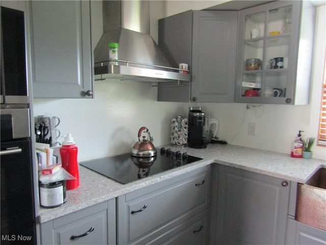 kitchen with light stone countertops, black electric stovetop, gray cabinetry, and wall chimney range hood