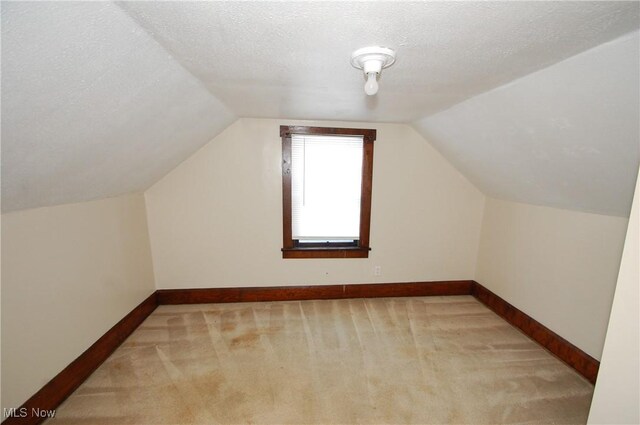 bonus room featuring lofted ceiling, light colored carpet, and a textured ceiling