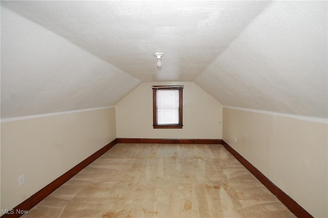 additional living space featuring light carpet, vaulted ceiling, and a textured ceiling