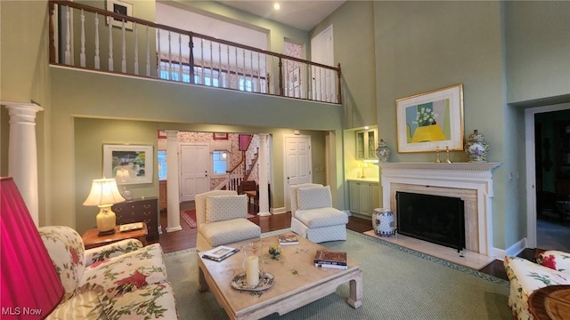 living area with baseboards, a fireplace with flush hearth, stairs, a high ceiling, and ornate columns