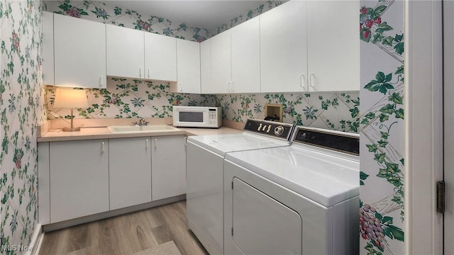 clothes washing area featuring cabinets, sink, washer and clothes dryer, and light hardwood / wood-style flooring