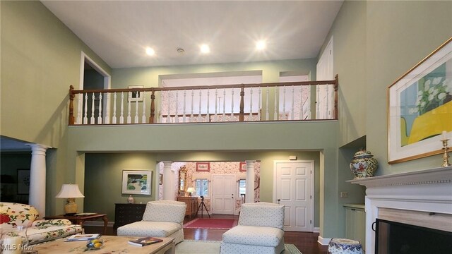 living area with dark wood-type flooring, a towering ceiling, a fireplace, and ornate columns