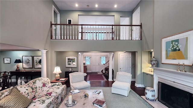 living room with a premium fireplace, wood finished floors, a towering ceiling, and ornate columns