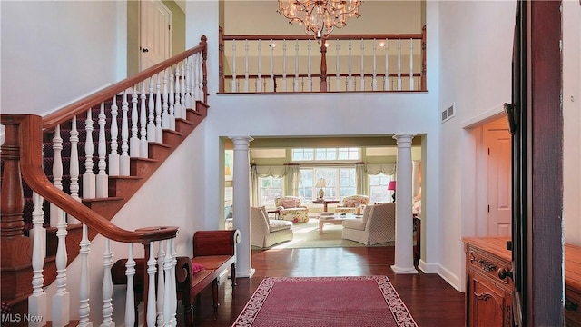 entrance foyer featuring dark wood-type flooring, decorative columns, a chandelier, and a high ceiling