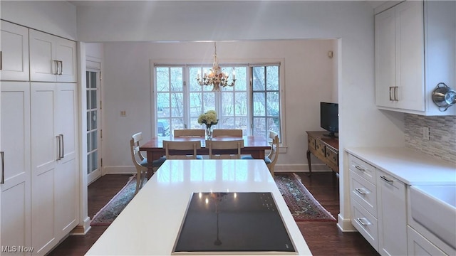 kitchen with dark wood-type flooring, white cabinetry, tasteful backsplash, a chandelier, and hanging light fixtures