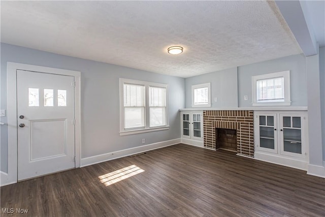 unfurnished living room featuring a brick fireplace, dark wood-type flooring, and a textured ceiling