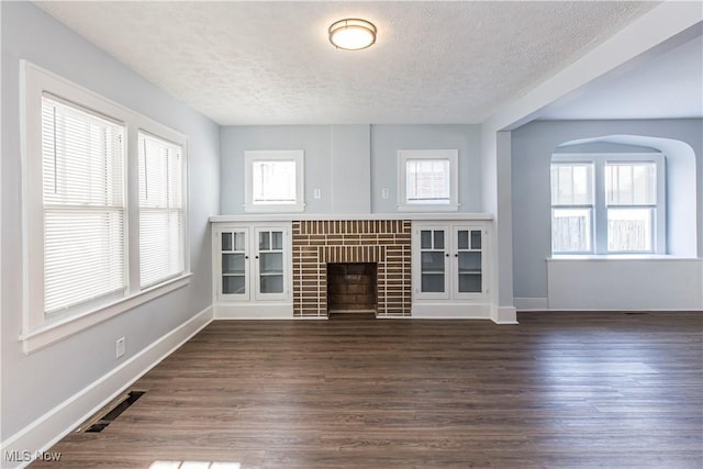 unfurnished living room with dark wood-type flooring, a brick fireplace, a healthy amount of sunlight, and a textured ceiling