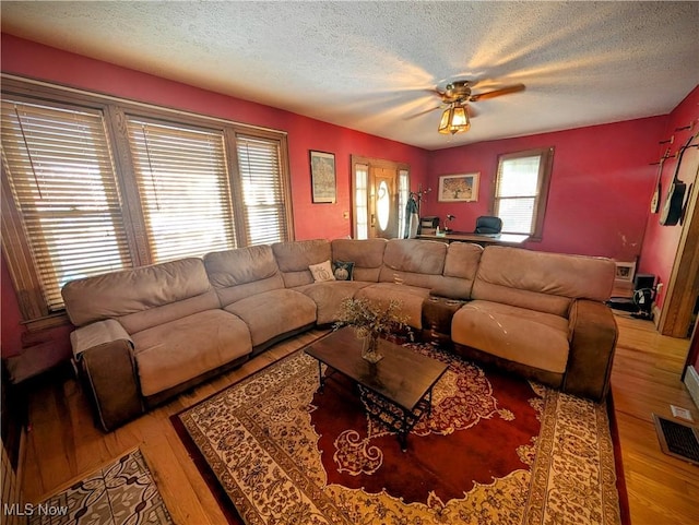 living room with ceiling fan, a textured ceiling, and light hardwood / wood-style floors