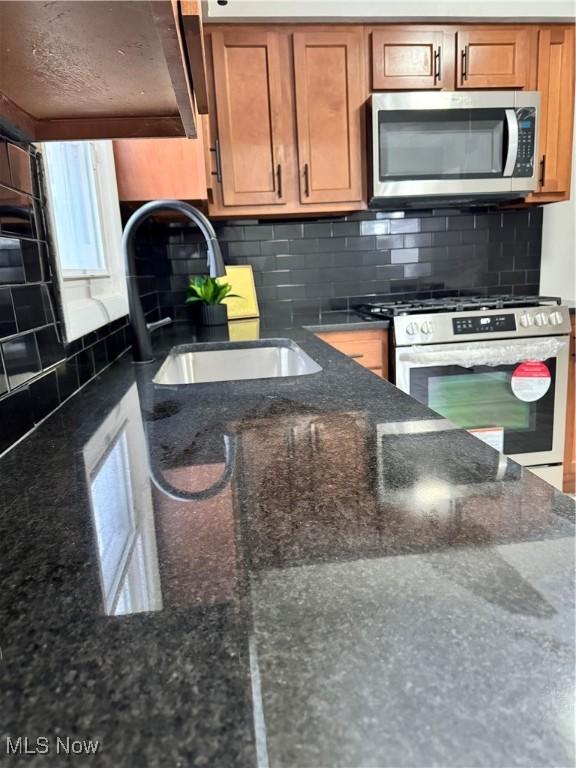 kitchen featuring backsplash, sink, appliances with stainless steel finishes, and dark stone counters