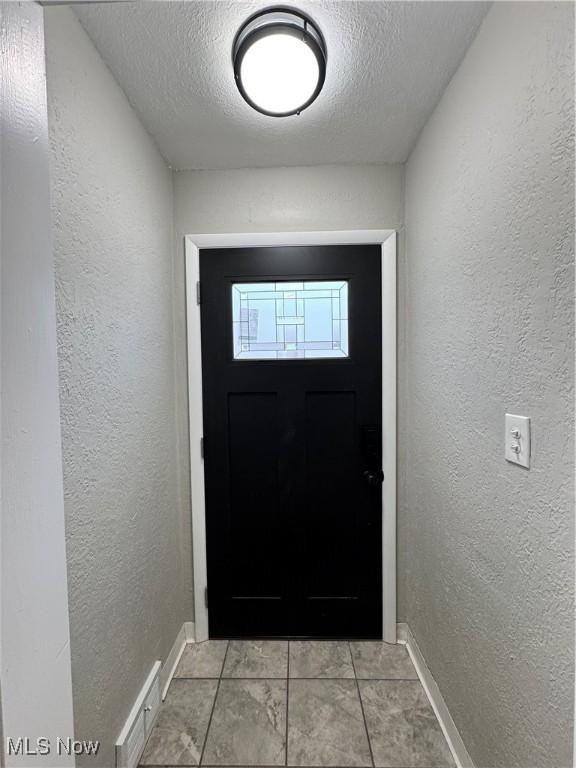 doorway with a textured ceiling and light tile patterned flooring