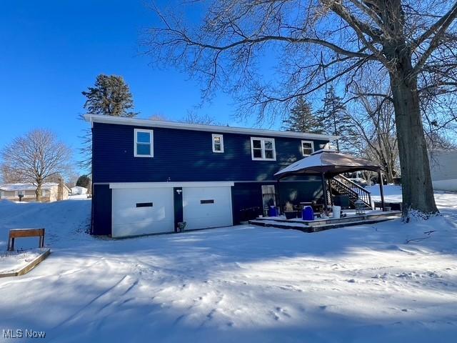 snow covered back of property featuring a garage