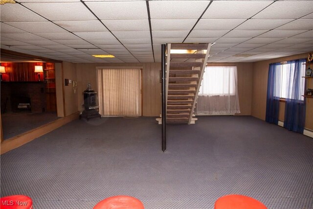 basement featuring dark carpet, a paneled ceiling, and wood walls