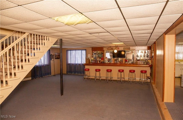 basement featuring carpet floors, a paneled ceiling, and indoor bar