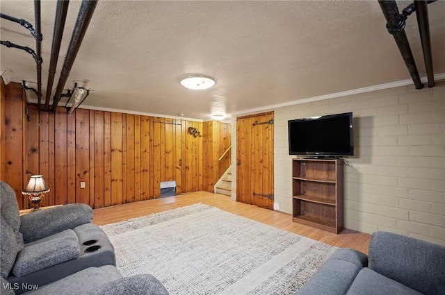 living room featuring hardwood / wood-style floors, ornamental molding, wood walls, and a textured ceiling