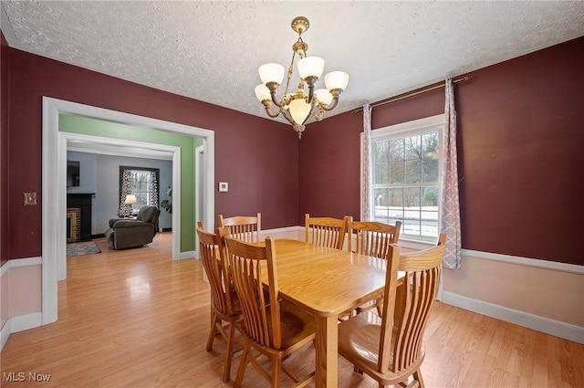 dining space featuring a textured ceiling, a brick fireplace, a chandelier, and light hardwood / wood-style flooring