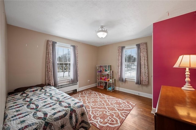 bedroom featuring wood-type flooring, multiple windows, radiator, and a textured ceiling