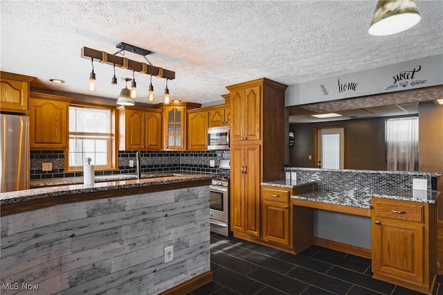 kitchen featuring stone counters, appliances with stainless steel finishes, sink, decorative backsplash, and hanging light fixtures