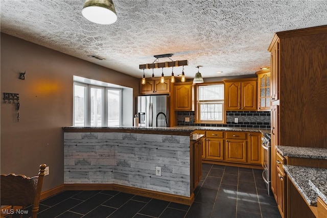 kitchen featuring dark tile patterned floors, appliances with stainless steel finishes, tasteful backsplash, decorative light fixtures, and dark stone counters