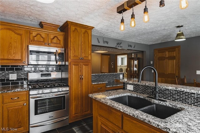 kitchen featuring stainless steel appliances, sink, light stone counters, and decorative light fixtures