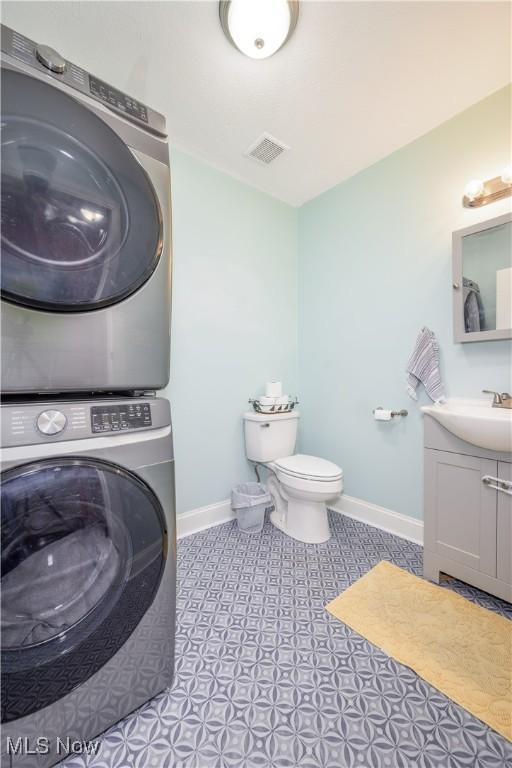 bathroom featuring toilet, stacked washer / dryer, and vanity