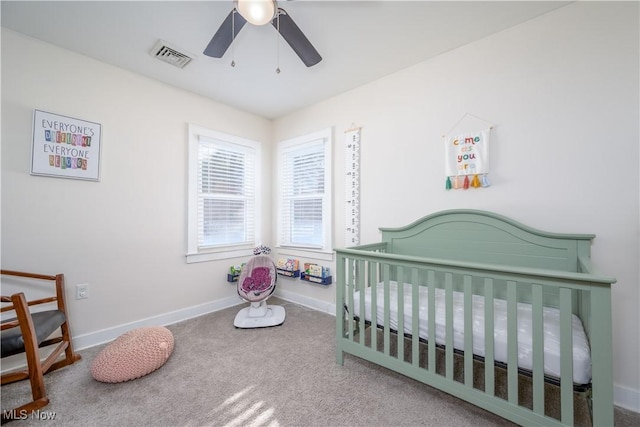 carpeted bedroom with ceiling fan and a crib