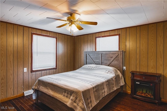 bedroom with ceiling fan, dark hardwood / wood-style floors, and wooden walls