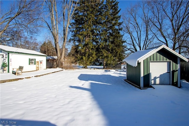 yard layered in snow featuring an outdoor structure and a garage