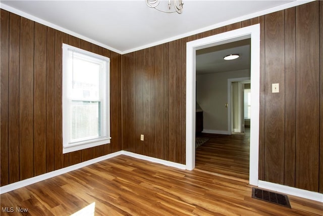 unfurnished room featuring baseboards, wood finished floors, visible vents, and wooden walls