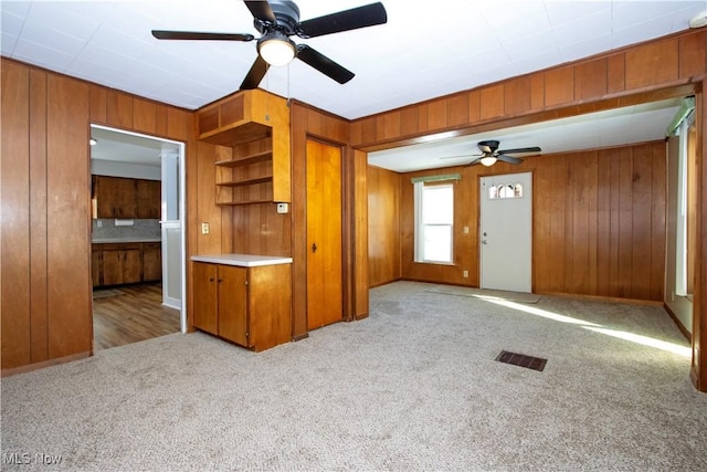 unfurnished living room with ceiling fan, light colored carpet, and wooden walls