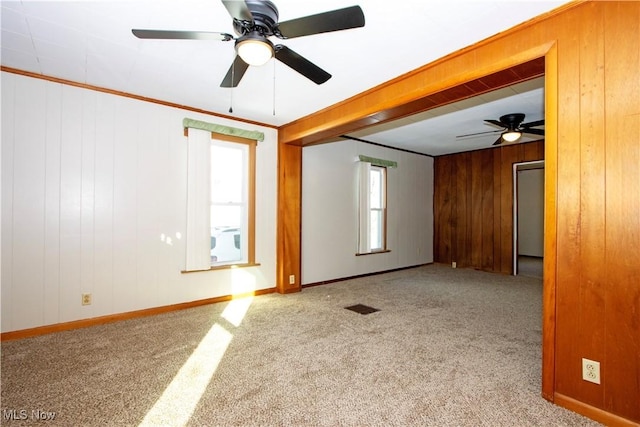 unfurnished room with light carpet, ceiling fan, wood walls, and ornamental molding