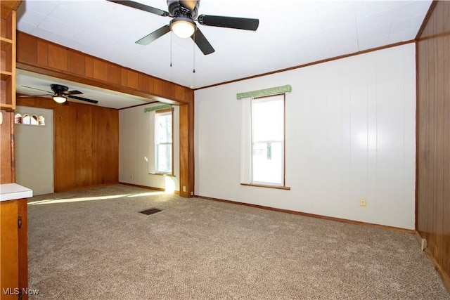 unfurnished room featuring light carpet, ceiling fan, crown molding, and wooden walls