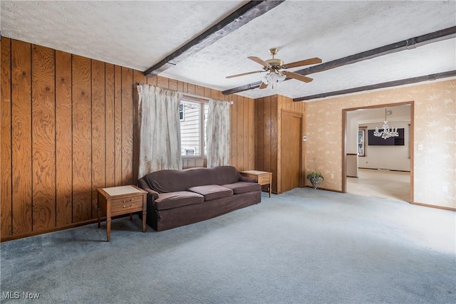 living room with ceiling fan with notable chandelier, a textured ceiling, wood walls, light colored carpet, and beam ceiling