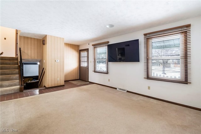 unfurnished living room with wood walls, a textured ceiling, and carpet flooring