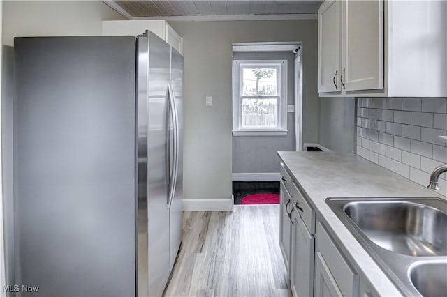 kitchen featuring decorative backsplash, sink, light hardwood / wood-style floors, stainless steel fridge, and wooden ceiling