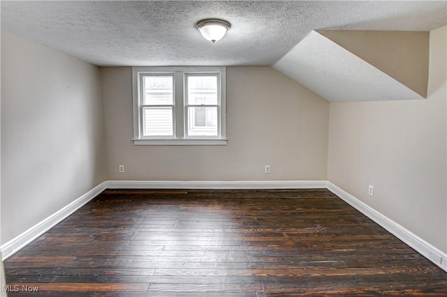 additional living space with a textured ceiling, dark hardwood / wood-style flooring, and vaulted ceiling