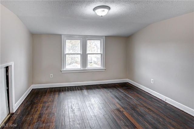 empty room with vaulted ceiling, dark hardwood / wood-style flooring, and a textured ceiling