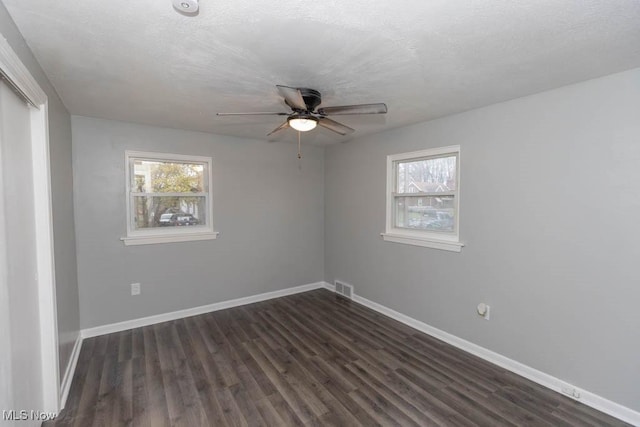 empty room featuring dark wood-type flooring, a wealth of natural light, a textured ceiling, and ceiling fan