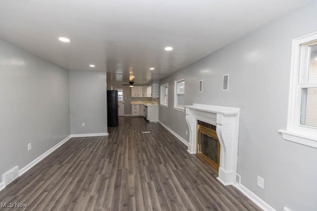 unfurnished living room featuring ceiling fan, dark hardwood / wood-style floors, and a healthy amount of sunlight