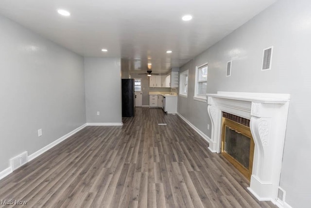 unfurnished living room with a tile fireplace, dark wood-type flooring, and ceiling fan