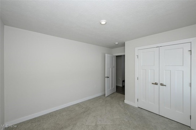 unfurnished bedroom featuring light colored carpet, a textured ceiling, and a closet