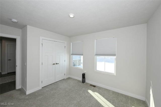 unfurnished bedroom featuring a textured ceiling, a closet, and light colored carpet