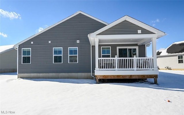 snow covered back of property featuring covered porch