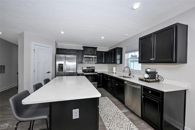 kitchen featuring hardwood / wood-style flooring, stainless steel appliances, a center island, a kitchen breakfast bar, and sink