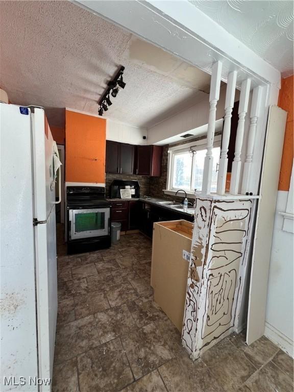 kitchen with white fridge, rail lighting, backsplash, dark brown cabinets, and sink