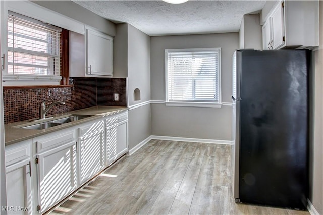 kitchen with white cabinetry, sink, stainless steel fridge, and light hardwood / wood-style floors